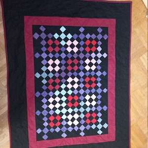 May include: A quilt with a black background and a burgundy border. The center of the quilt is a patchwork of small squares in shades of red, blue, purple, and white.