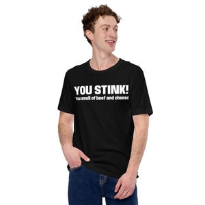 May include: A black t-shirt with the text "YOU STINK! You smell of beef and cheese!" printed in white.