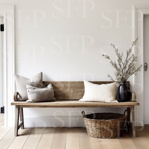 May include: A rustic wooden bench with a natural wood finish, featuring a woven wicker basket and two throw pillows. The bench is placed in a white room with a vase of dried branches.