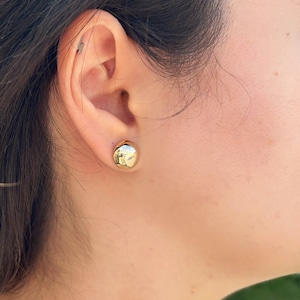 May include: A pair of gold-toned round stud earrings. The earrings are small and simple, and they are a classic style that can be worn with any outfit.