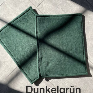 Peut inclure: Deux sets de table rectangulaires en tissu vert fonc&eacute; avec un bord cousu. Les sets de table sont sur un sol en carrelage gris.