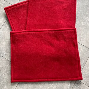 Peut inclure: Trois sets de table en polaire rouge avec un bord cousu. Les sets de table sont empil&eacute;s les uns sur les autres. Le mot "Rot" est &eacute;crit en noir sous les sets de table.