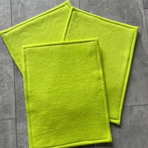 May include: Three green felt squares with stitched edges. The squares are stacked on top of each other. The bottom square has the word "Apfelgrün" written in black below it.
