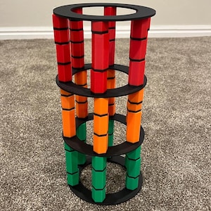 May include: A colorful, geometric sculpture with a cylindrical design. The structure features three black circular tiers connected by vertical columns in red, orange, and green. The columns are segmented with black accents.