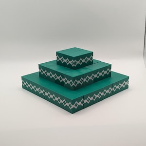 May include: A tiered structure composed of green blocks, each adorned with a repeating silver diamond pattern. The blocks are arranged in a pyramid shape, with the largest base at the bottom and decreasing in size towards the top.