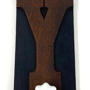 May include: A wooden wall decor with a black and brown paint design. The decor features a carved letter "Y" and a white ceramic knob with a gold center.