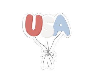 May include: A sticker featuring the letters "USA" in red, white, and blue, designed to look like balloons. The letters are outlined in white and connected by thin black lines tied together with a bow.