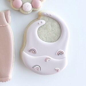 May include: A pink baby bib cookie decorated with small rainbow designs.
