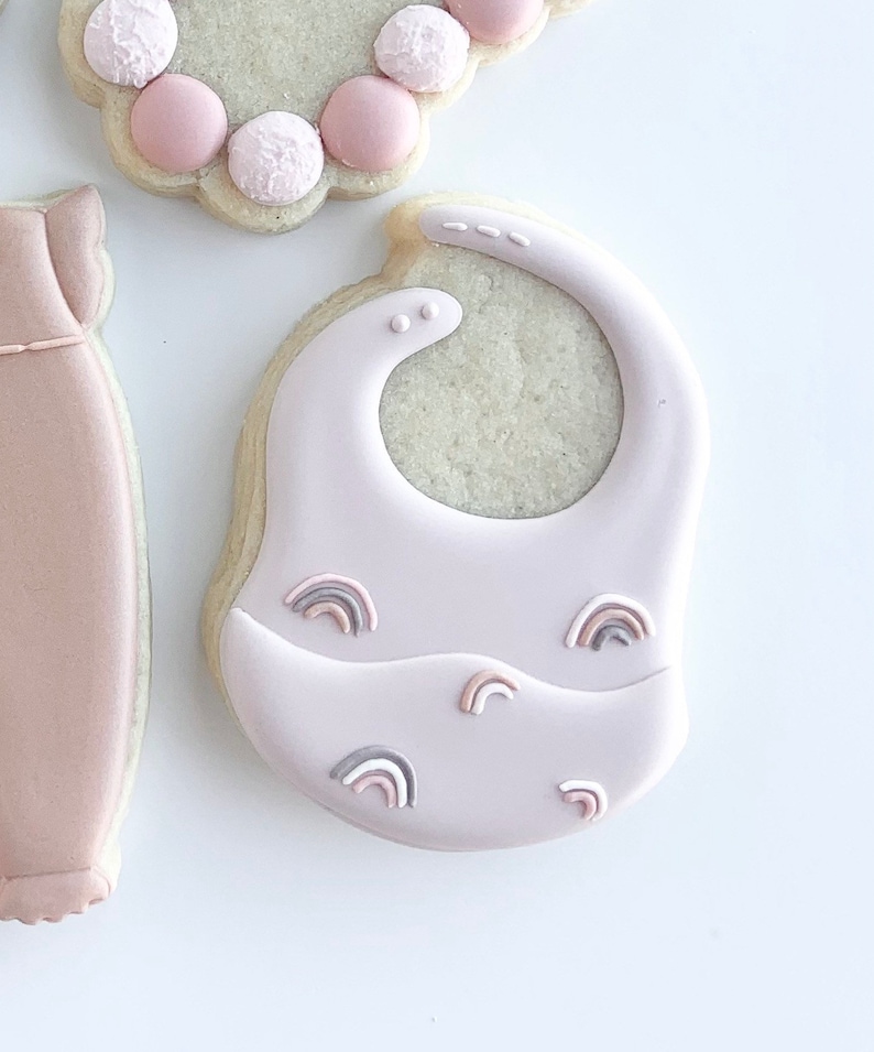 May include: A pink baby bib cookie decorated with small rainbow designs.