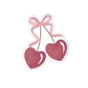 Puede incluir: Dos cerezas rojas en forma de corazón con una cinta rosa atada en la parte superior de los tallos.