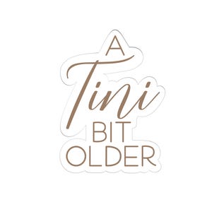 Puede incluir: Una pegatina blanca con texto marrón que dice "A Tini Bit Older".