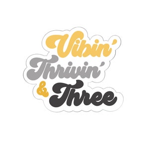 Puede incluir: Una pegatina con el texto "Vibin' Thriwin' & Three" en una fuente retro. Las palabras están en amarillo, gris y negro.