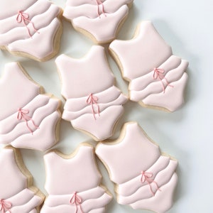 May include: Nine pink sugar cookies decorated with white icing and pink bows. The cookies are shaped like a one-piece swimsuit.