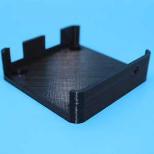 May include: A black plastic 3D printed box with a square base and a rectangular opening on one side.