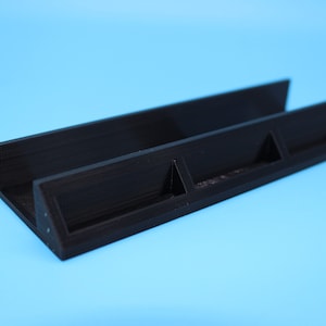 May include: A black plastic stand with three slots for holding game cards. The stand is angled and has a textured surface.