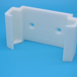 May include: White plastic wall mount with two holes for screws. The mount has a U-shaped opening for holding an object.