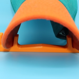 May include: Orange plastic hat rack with a teal and orange baseball cap on top.