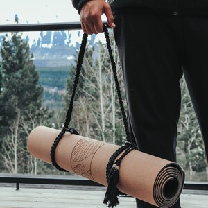 Pu&ograve; includere: Un tappetino da yoga in sughero arrotolato con un cinturino nero e nappe. Il tappetino ha un motivo floreale stampato.
