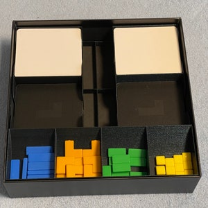 Könnte beinhalten: Eine schwarze Aufbewahrungsbox mit Fächern zur Organisation von Kleinteilen. Die Box enthält blaue, gelbe und grüne Plastikteile.