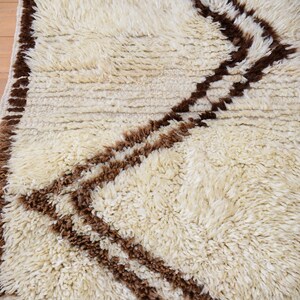 May include: A white shag rug with a brown geometric pattern. The rug has a fringe border.
