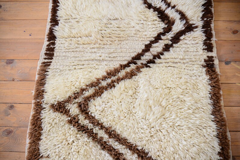 May include: A white shag rug with a brown geometric pattern. The rug has a fringe border.