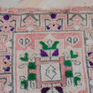 Puede incluir: Una alfombra rosa y blanca con un patr&oacute;n geom&eacute;trico. La alfombra tiene detalles verdes y morados.