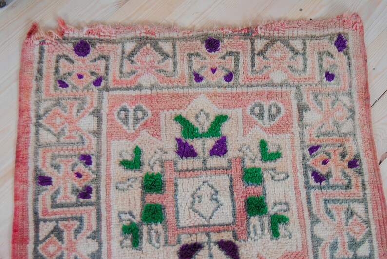 Puede incluir: Una alfombra rosa y blanca con un patr&oacute;n geom&eacute;trico. La alfombra tiene detalles verdes y morados.