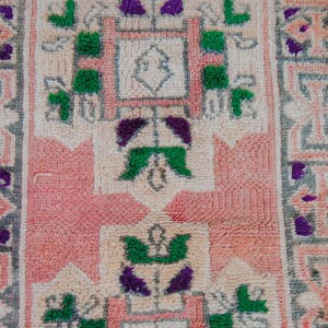 Puede incluir: Una alfombra rosa y crema con un patr&oacute;n geom&eacute;trico en tonos de verde y morado. La alfombra tiene un dise&ntilde;o central con una forma cuadrada y un cuadrado m&aacute;s peque&ntilde;o en el centro.