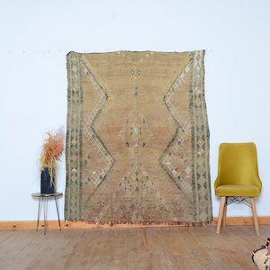 May include: A rectangular area rug featuring a warm, golden-brown base color with a large, central diamond-shaped geometric pattern outlined in dark green and white. The rug displays intricate, symmetrical tribal-inspired motifs throughout.