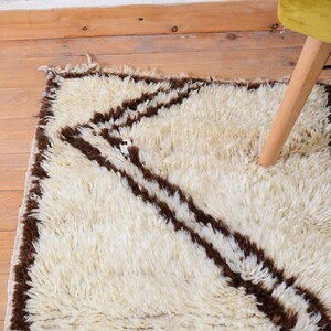 May include: A white shag rug with brown stripes. The rug has a geometric pattern and is made of soft, fluffy fibers.