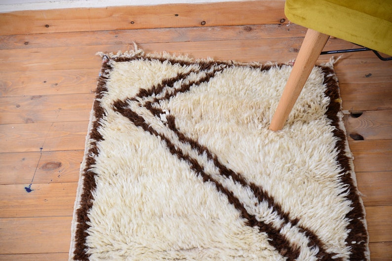 May include: A white shag rug with brown stripes. The rug has a geometric pattern and is made of soft, fluffy fibers.