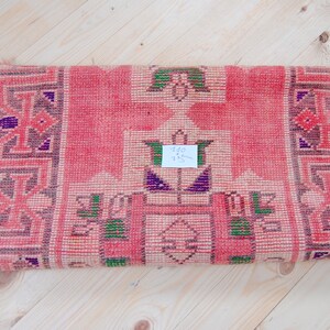 Puede incluir: Una alfombra tejida rosa y blanca con un patr&oacute;n geom&eacute;trico. La alfombra tiene una etiqueta de precio que dice "10 &euro; 15 &euro;".