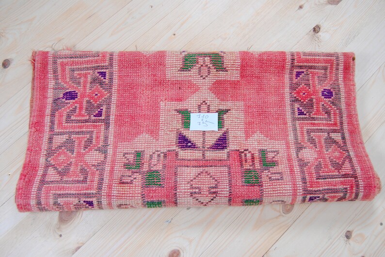 Puede incluir: Una alfombra tejida rosa y blanca con un patr&oacute;n geom&eacute;trico. La alfombra tiene una etiqueta de precio que dice "10 &euro; 15 &euro;".