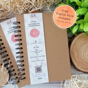 Op de afbeelding: A5 spiraalgebonden notitieboeken met kraftpapieren kaften. De notebooks hebben een wit label met de tekst "SPIRAL NOTEBOOK" en "A5". Het label bevat ook de tekst "Hard Kraft Cover", "100 Pages" en "50 Colored Sheets (180gsm)". Een ronde sticker zegt "Free Digital Pack Included".