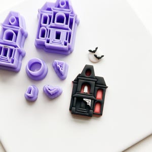 Può includere: Una collezione di formine e decorazioni a tema Halloween. Include formine viola a forma di casa, una casa infestata nera e rossa e una piccola decorazione con pipistrelli e una luna. Perfetto per creare dolcetti spettrali.