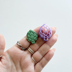 May include: A green artichoke shaped polymer clay charm and a purple artichoke shaped polymer clay mold.