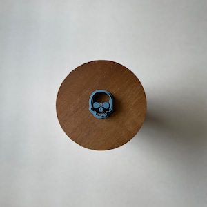 May include: A blue plastic skull cookie cutter on a wooden surface.