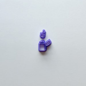 May include: Purple plastic cookie cutter shaped like a lighter with a flame on top.