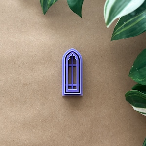 Puede incluir: Un cortador de galletas de plástico morado con forma de ventana arqueada con un patrón de rejilla.