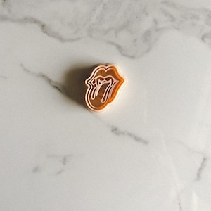 May include: A brown plastic cookie cutter shaped like the Rolling Stones tongue logo.