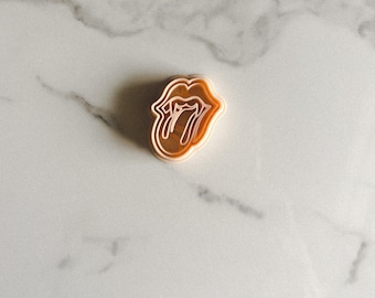 May include: A brown plastic cookie cutter shaped like the Rolling Stones tongue logo.