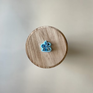 Op de afbeelding: Een blauwe plastic koekjesvormer in de vorm van een gestileerde wolk op een houten oppervlak.