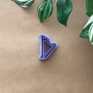 May include: Purple plastic cookie cutter shaped like a harp. The harp has a curved top and strings.