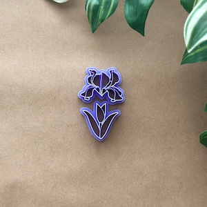 May include: Purple plastic cookie cutter shaped like an iris flower with a single stem and leaves.