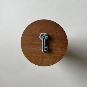 May include: A black and white key-shaped cookie cutter on a wooden surface.