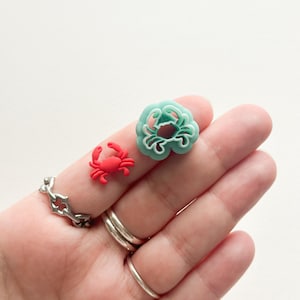 May include: Two small plastic crab-shaped cookie cutters. One is red and the other is light blue.
