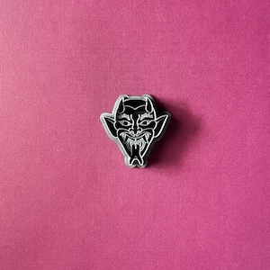 May include: Black and white enamel pin featuring a cartoon devil with horns and a menacing expression.