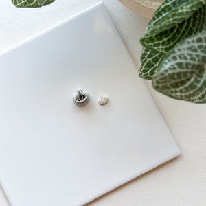 Könnte beinhalten: Zwei Keramik-Knoblauch-Anhänger, einer größer und einer kleiner, auf einer weißen Fliesenfläche. Der größere Anhänger ist grau mit schwarzen Details, während der kleinere Anhänger weiß ist.