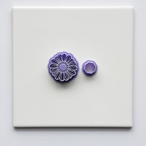 May include: Two purple plastic cookie cutters, one shaped like a flower and the other a circle.