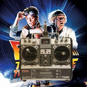 Könnte beinhalten: Ein Futaba-Funkfernsteuersender ist vor einem Filmplakat für „Zurück in die Zukunft“ abgebildet. Das Plakat zeigt die Stars des Films und einen DeLorean. Der Sender hat Drehregler, Schalter und ein digitales Display.